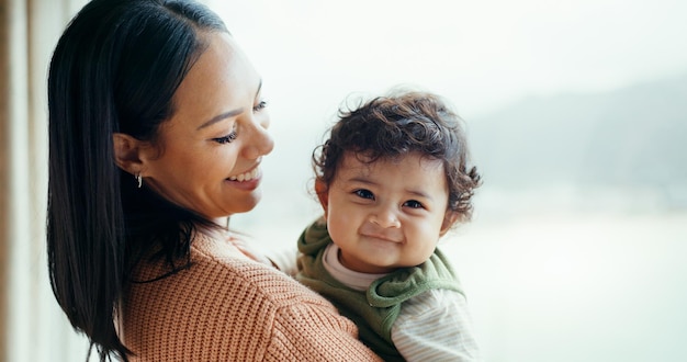 Mother newborn and smile by window home and happy together with care love and bonding in childhood Mom infant baby and excited with connection development and hug at family house in Canada