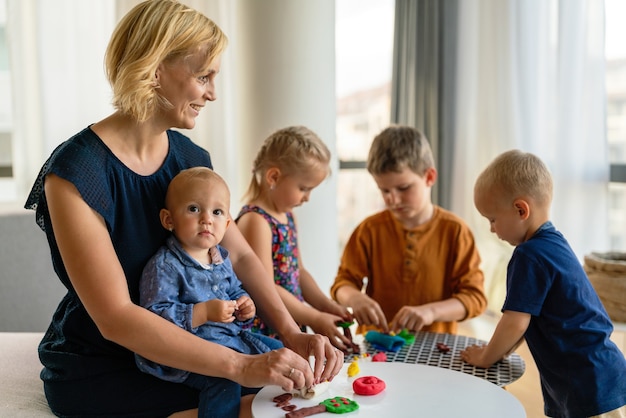 Photo mother or nursery teacher teaches her children to work with colorful play clay toys. children creativity concept