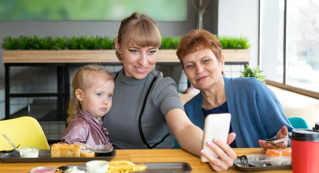 Mother photographing through phone while sitting with daughter and senior woman