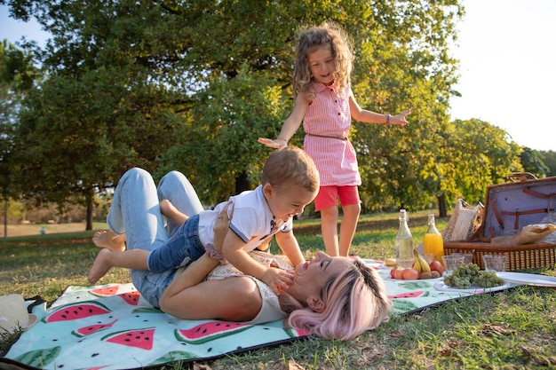 Mother at a picnic plays with her children lifts her son while her daughter watches