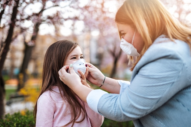 Mother placing protective mask on face of her daughter. Coronavirus, Covid-19 concept.