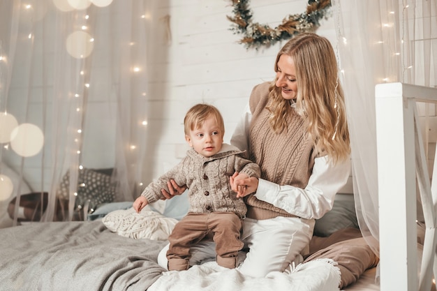 La mamma gioca e si diverte con il suo figlioletto su un letto a baldacchino in stile boho con bokeh. maternità e trascorrere del tempo con un bambino durante la quarantena del coronavirus.