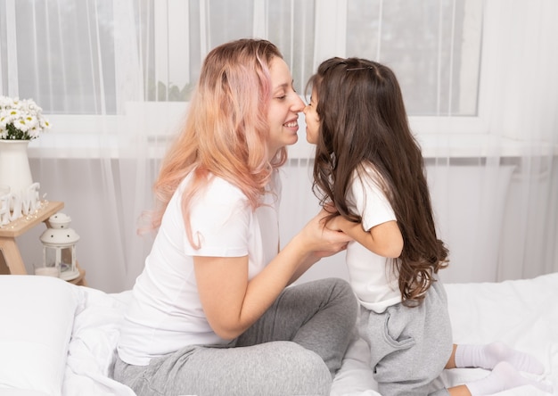 Mother play with little active daughter in bed at home, having fun, activity with children.