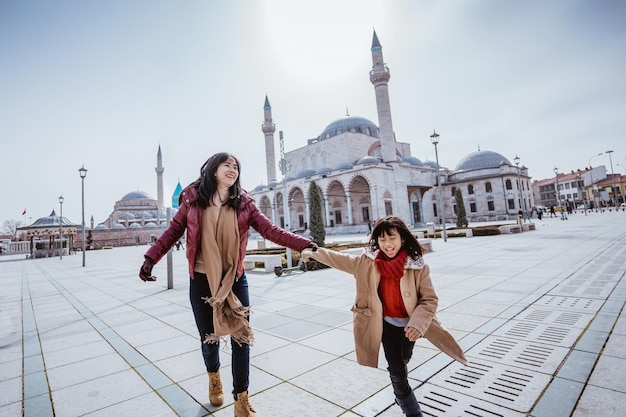 Photo mother playing around with her daughter in the square while visiting mosque in konya turkiye
