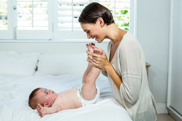 Mother playing with baby boy lying on bed