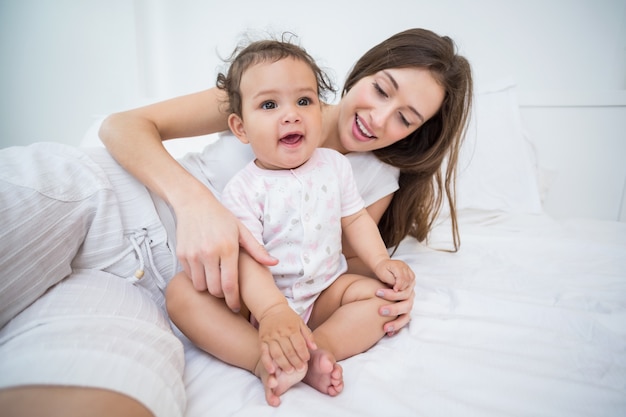 Mother playing with baby girl on bed 