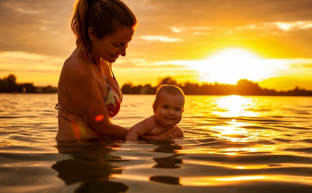 Mother playing with baby in water during sunset.