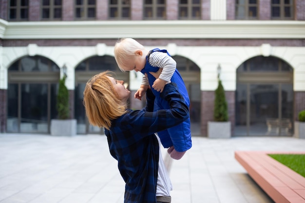 Mother playing with child baby boy in stylish clothes outdoors on urban background