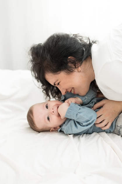 Mother plays with the baby on the bed. Mother tickles her son.