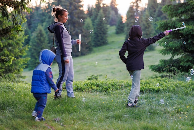 Mother plays with daughter and son in soap bubbles in a forest during an walk