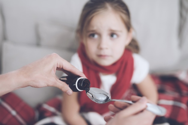 Mother pour the syrup into the spoon for sick girl.