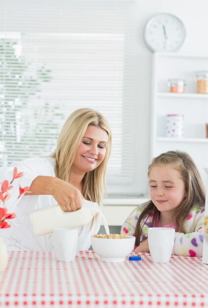 mother pouring milk into cereal bowl for daughter