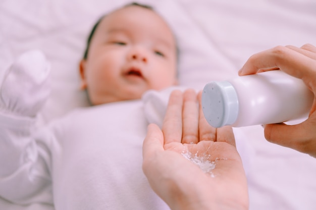 Mother preparing baby powder in her hand and 2 months old baby boy on bed.