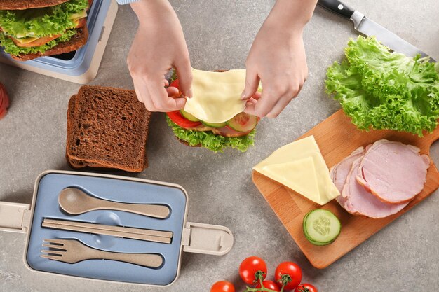 Mother preparing sandwich for school lunch on table