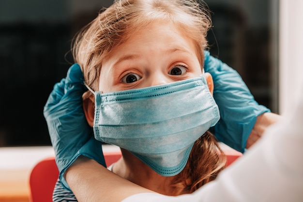 La madre indossa la mascherina medica sterile del suo bambino. bambina e mamma in mascherina medica. vaccinazione dei bambini