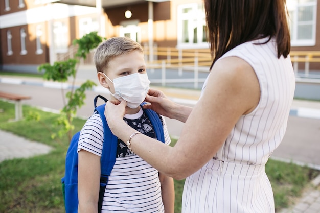 어머니는 학교에 갈 준비를 하기 위해 Covid-19 또는 코로나바이러스 발병을 보호하기 위해 아들의 얼굴에 안전 마스크를 씁니다. 학교 개념으로 돌아가기. 코로나바이러스를 예방하기 위한 의료용 마스크.