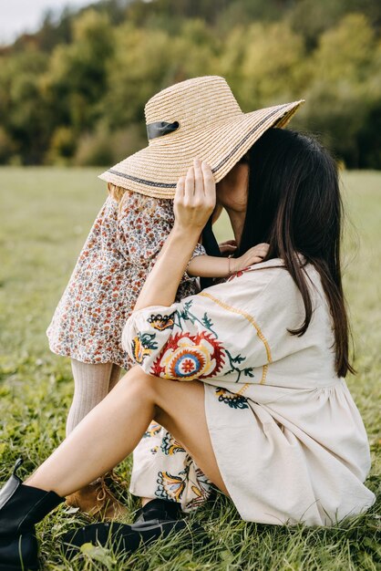 Mother putting on little girl her big straw hat and kissing her nose