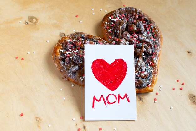 Mother's day card with a red heart over a chocolate heart shaped cake on wooden table