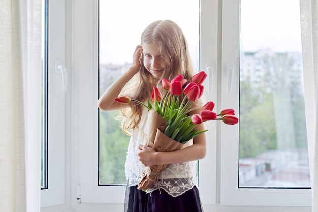 Mother's day girl child with bouquet of red tulips flowers at home