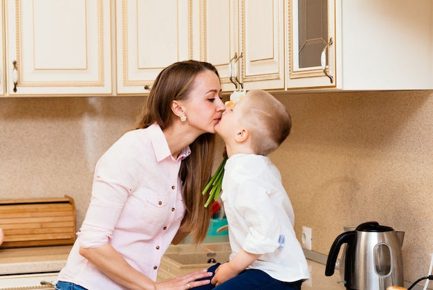 Mother's day, holidays and family concept - happy little son gives flowers to his smiling mother at home. A child gives mom a bouquet of daffodils