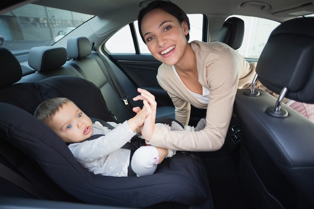 彼女の赤ん坊を車の座席に固定している母