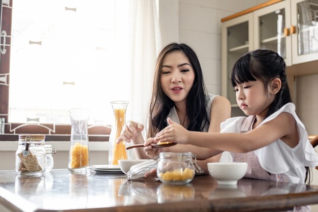 Mother sit looking at the daughter playing in the kitchen.