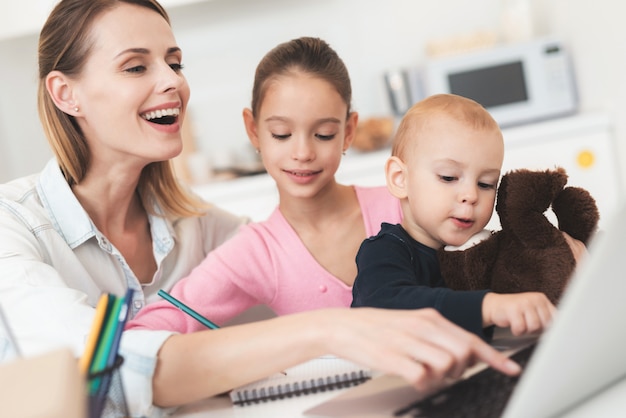 Mother sits next to them and they are sitting at computer.