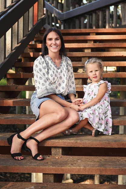 The mother sits with her daughter on the steps of a wooden staircase Mother's Day