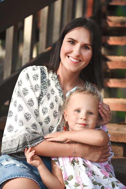 The mother sits with her daughter on the steps of a wooden staircase Mother's Day