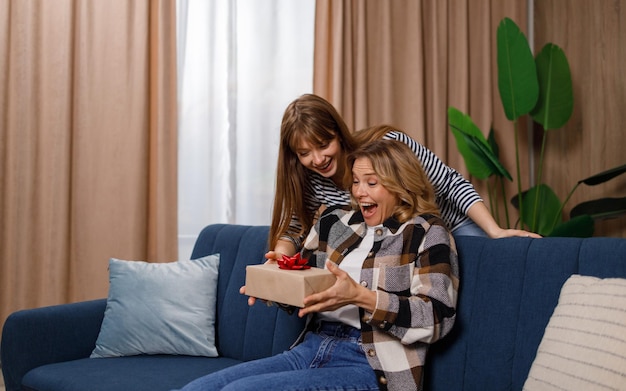 Mother sitting on the couch in the living room is delighted\
with her daughter\'s gift