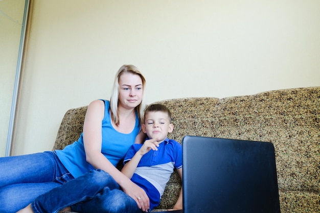 Madre, bambino piccolo, ragazzo a casa seduto sul divano, utilizzando il laptop. formazione online, shopping, video