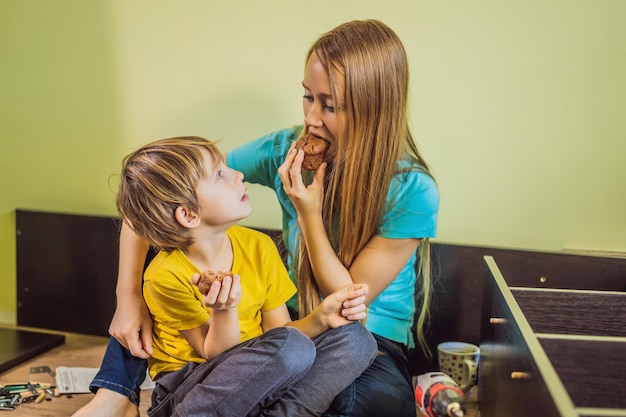 母と息子が家具を組み立てる彼らは休憩を取り、カップケーキを食べる少年は家で母親を助ける幸せな家族のコンセプト