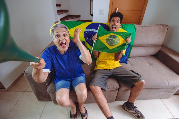 브라질을 응원하는 TV를 보며 거실에서 컵을 축하하는 어머니와 아들