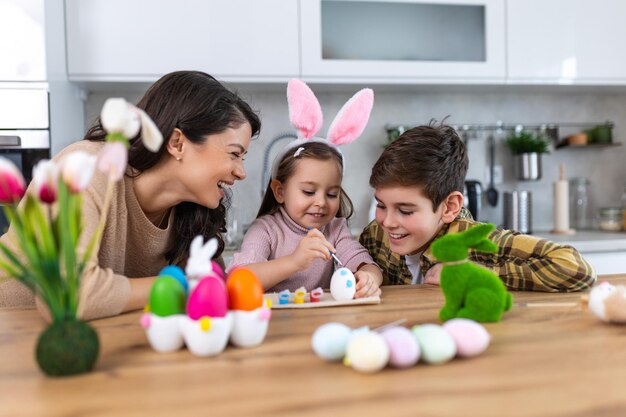 Foto madre, figlio e figlia festeggiano la pasqua, colorano le uova, feste familiari felici, una bambina carina con le orecchie di coniglio che ride, sorride e si diverte.