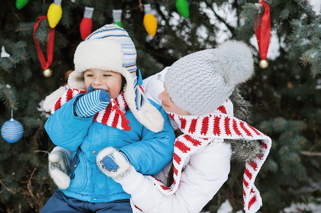 母と息子は冬の公園で屋外のクリスマスツリーを飾る、