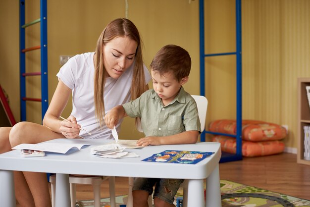 Mother and son draw at a table inside the room.