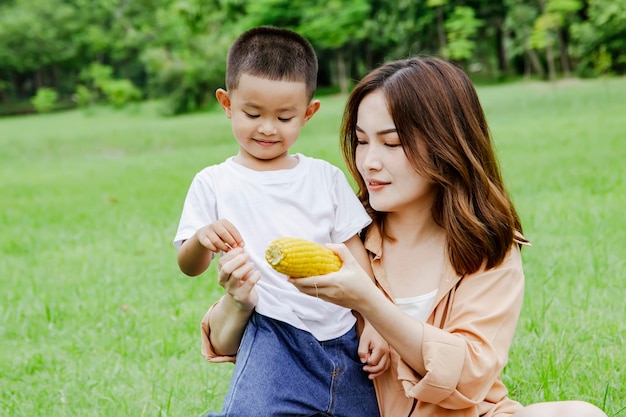 Mother and son eat delicious boiled corn in the grass garden during a weekend camping trip.