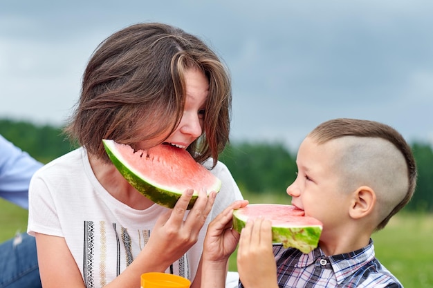 牧草地や公園でスイカを食べる母と息子ピクニック屋外の肖像画で幸せな家族小さな男の子とお母さん