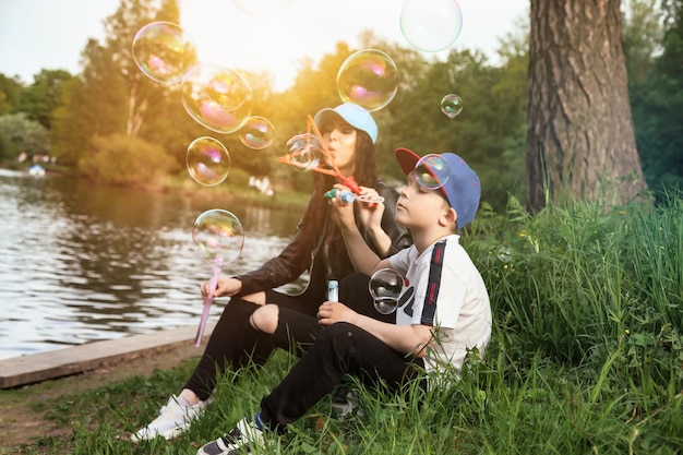 Мать и сын веселятся на зеленой лужайке с мыльными пузырями в весеннем общественном парке вместе в солнечный день