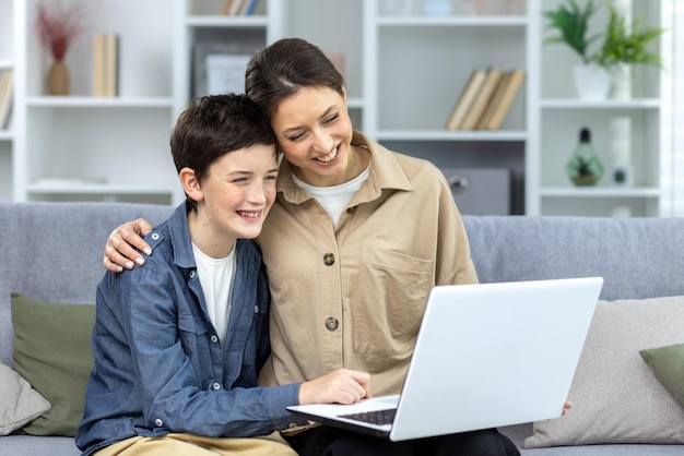mother and son hugging together sitting on sofa at home in living room watching video online using