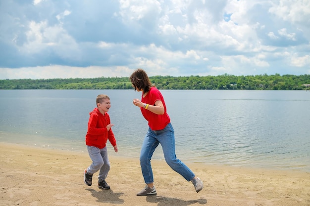 A mother and son laugh on the beach in front of a lake.