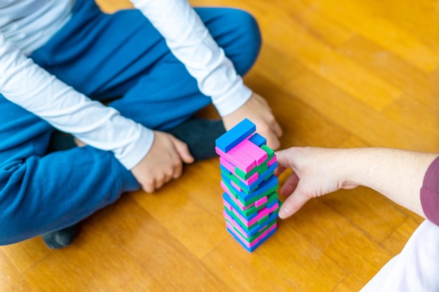 Мать и сын играют в разноцветные деревянные блоки, играя в башню для детей на полу