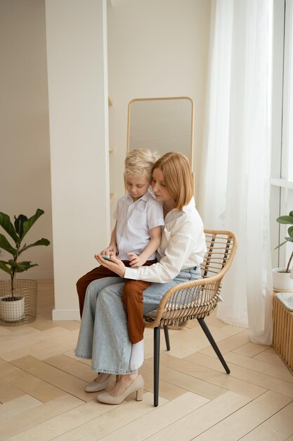 Mother and son playing with mobile phone while sitting in chair at home