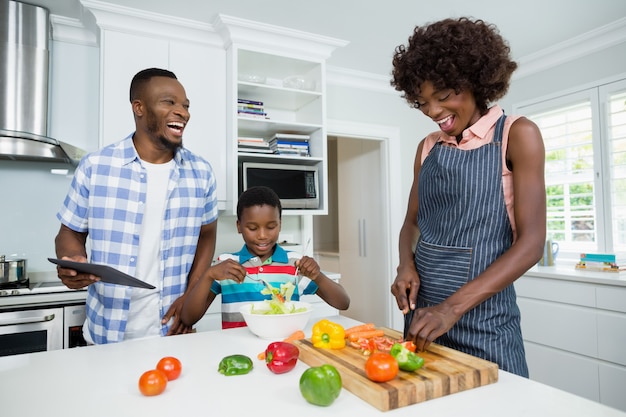 Mother and son preparing salad while father using digital tablet in kitchen