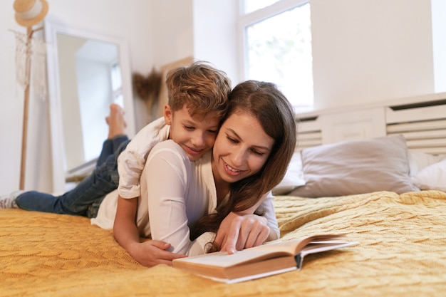 Mother and son reading a book while lying on the bed at home