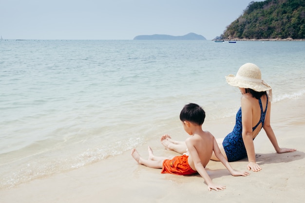 Una madre e un figlio si rilassano e si siedono sulla spiaggia e sul mare all'aperto al cielo blu