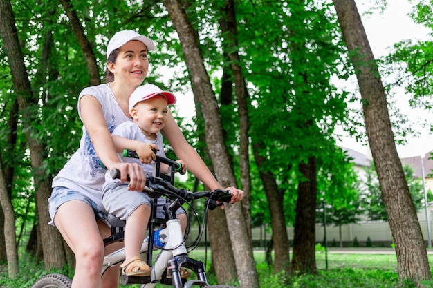 母と息子が自転車に乗る、母は夏に公園の自転車で子供用の椅子に子供を運ぶ