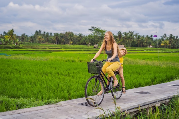 Mother and son ride a bicycle on a rice field in ubud bali travel to bali with kids concept