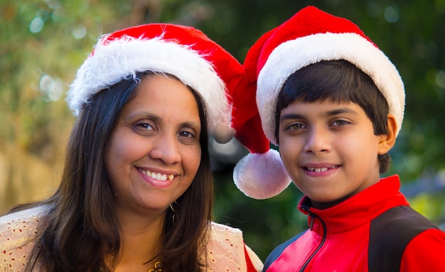 Mother and son in Santa hats smiling and looking at camera during Christmas Season 