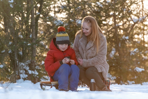 Mother and son sitting on a sled in the winter forest Happy family playing in the snow